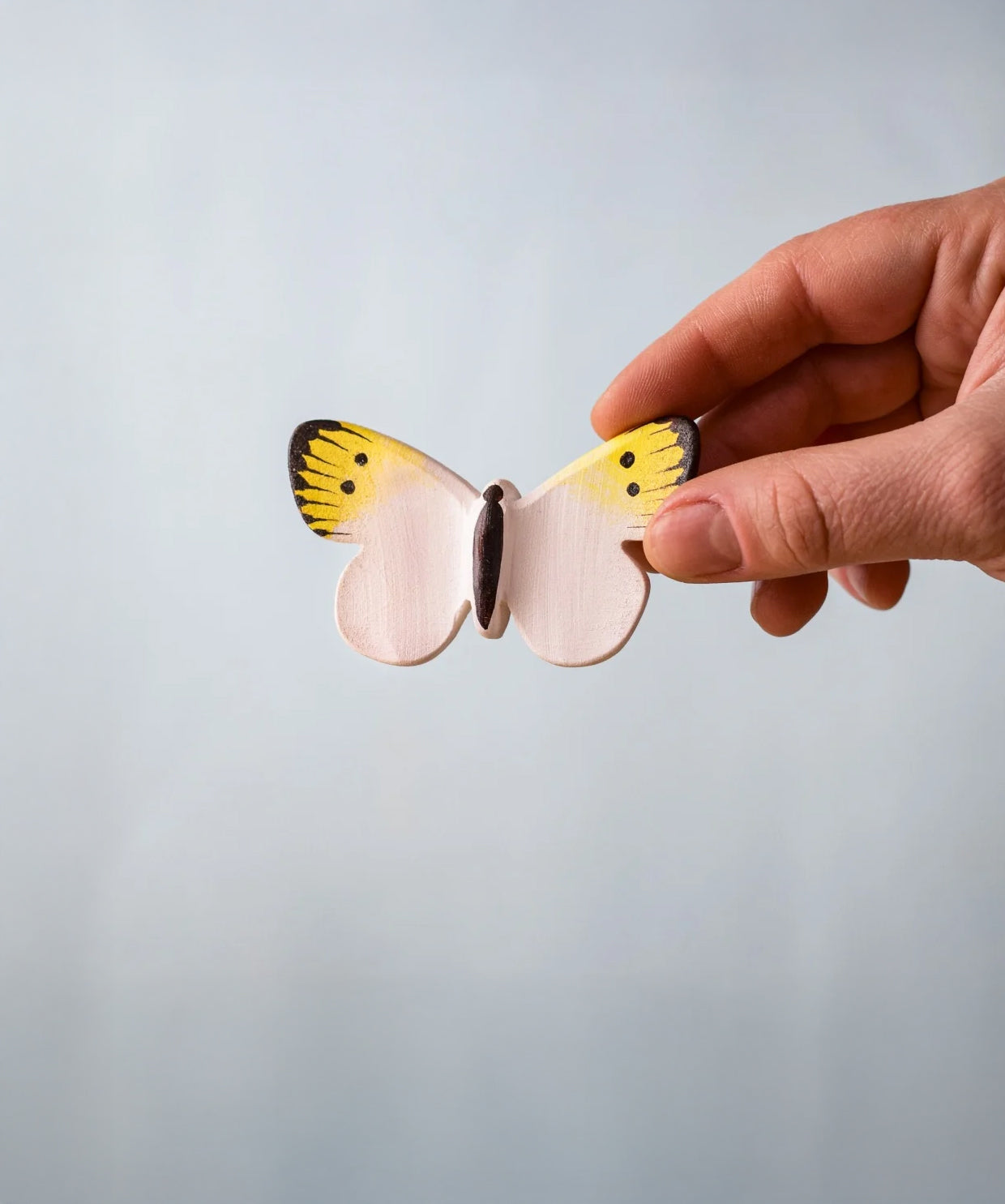 Bumbu Toys Wooden Butterfly in Yellow, being held in an adult's hand.