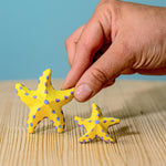 A close up of an adult's hand holding on to the large starfish from the Bumbu yellow starfish set.