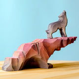 A wold stoof on top of a Bumbu wooden howling stone on a wooden surface against a blue background. 
