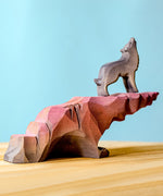 A wold stoof on top of a Bumbu wooden howling stone on a wooden surface against a blue background. 