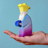 Bumbu Wooden Nativity Figure - Three Kings Melchior on an adults hand with blue background.