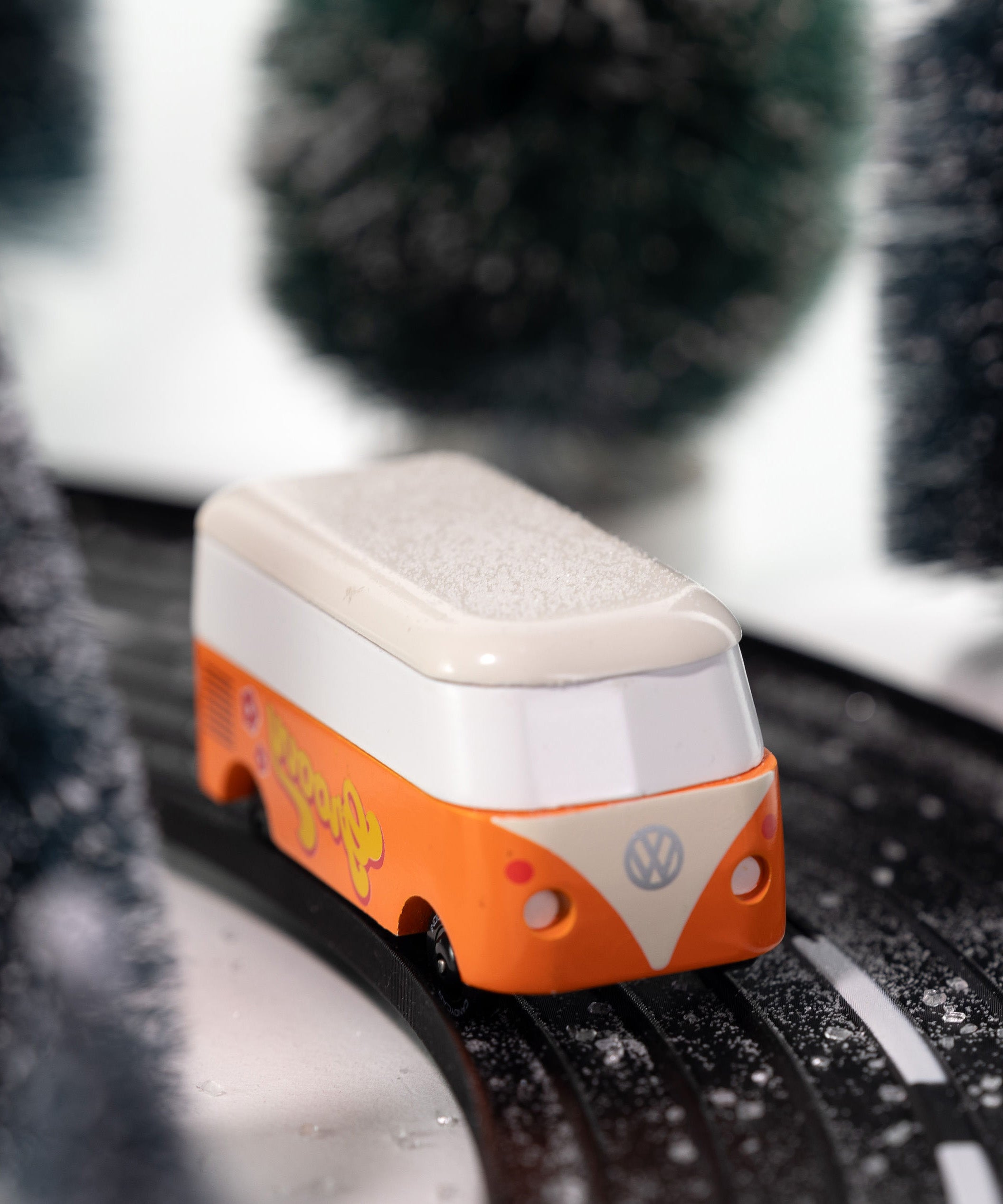 Front view of CandyLab orange VW T1 Campervan with 'Groovy' text on the side in a 60s font - driving through a snowy forest. 