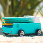 Close up of a candylab wooden beach van toy vehicle on some sand with mini surfboard toys on the back