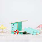 Candylab childrens wooden beach tower toy on some white sand next to some miniature umbrellas