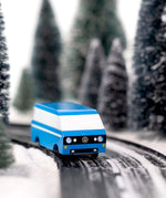 CandyLab blue VW T3 CandyVan with white stripe on the side - front view on a road through a wintry forest.