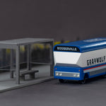 Candylab handmade wooden diecast bus toy on a grey background next to a miniature bus stop