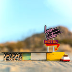 Close up of the Candylab wooden luggage wagon toy parked outside the wooden toy motel on a sandy surface