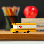 Candylab wooden bus vehicle toy on a wooden desk in front of some books and a red apple