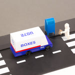 Close up of a Candylab wooden post van next to a toy mailbox and toy figure on a black rubber road