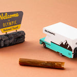 Candylab childrens wooden rv van toy on an orange background next to a toy rock and log