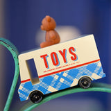 CandyLab cream and blue CandyVan with a brown teddy bear on the roof with Toys text logo in red on the side - placed on a chair frame with a faded blue background.