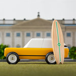 Candylab cotswold gold toy car on a green background with a miniature wooden surfboard in front of a palace model