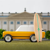 Candylab cotswold gold toy car on a green background with a miniature wooden surfboard in front of a palace model
