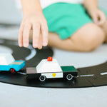 Close up of a childs hand pushing the candylab handmade wooden police car on a black rubber road