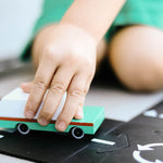 Close up of a childs hand pushing the Candylab solid wooden teal wagon toy on a black road set