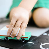 Close up of a childs hand pushing the Candylab solid wooden teal wagon toy on a black road set