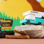 Candylab wooden campervan toy on top of a grey rock in front of a colourful mountain background