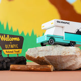 Candylab wooden campervan toy on top of a grey rock in front of a colourful mountain background