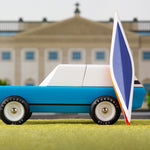 Candylab blue wooden suv toy with a miniature wooden kayak on a green background in front of a model palace