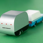 Close up of the Candylab small wooden Airstream toy connected to a blue car toy on a green background