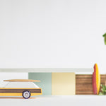 Candylab solid wooden car toy in front of a miniature waldorf shack in some wooden surfboards