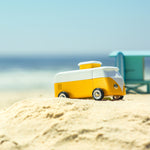Close up of a wooden Candylab vw campervan toy on a sandy beach in front of a blue sky