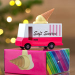 Candylab pink and white toy ice cream truck on top of its cardboard box in front of some Christmas lights