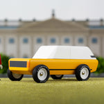 Toy figure stood on a green background next to the Candylab childrens handmade cotswold suv toy car