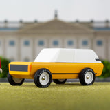 Toy figure stood on a green background next to the Candylab childrens handmade cotswold suv toy car
