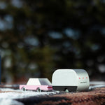 Close up of a childrens candylab airstream and pink sedan toy on a brown blanket in front of a camping mug and lamp