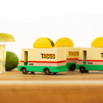 Close up of 3 wooden Candylab taco vans on a wooden table next to a glass