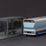Candylab Tiny Town toy bus on a grey background next to a miniature bus stop