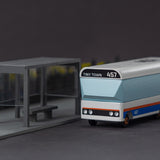 Candylab Tiny Town toy bus on a grey background next to a miniature bus stop