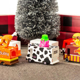 6 wooden Candylab toy trucks lined up on a brown carpet in front of a Christmas tree and some red presents