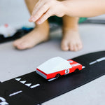Close up of the Candylab red racing car toy on a rubber road set in front of a childs feet