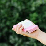 Close up of a childs hand holding the Candylab solid wooden pink sedan car on a green background