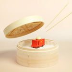Candylab wooden dumpling toy truck inside a round wooden box next to some chopsticks on a beige background