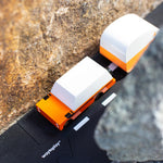 Orange suv diecast toy car pulling an orange caravan toy between two large rocks