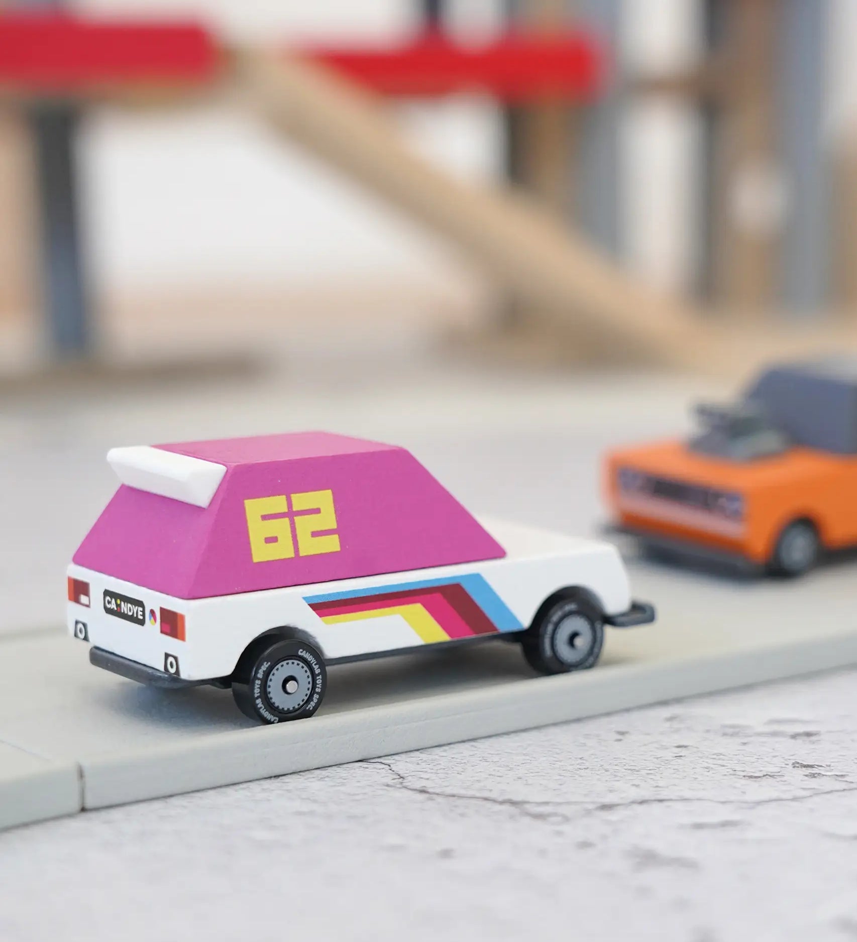Candylab wooden diecast pink 62 racer toy car on a play road with another car in the background