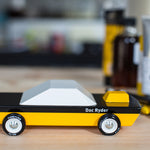 Candylab Doc Ryder toy muscle car on a wooden table in front of a stack of pencils and paints