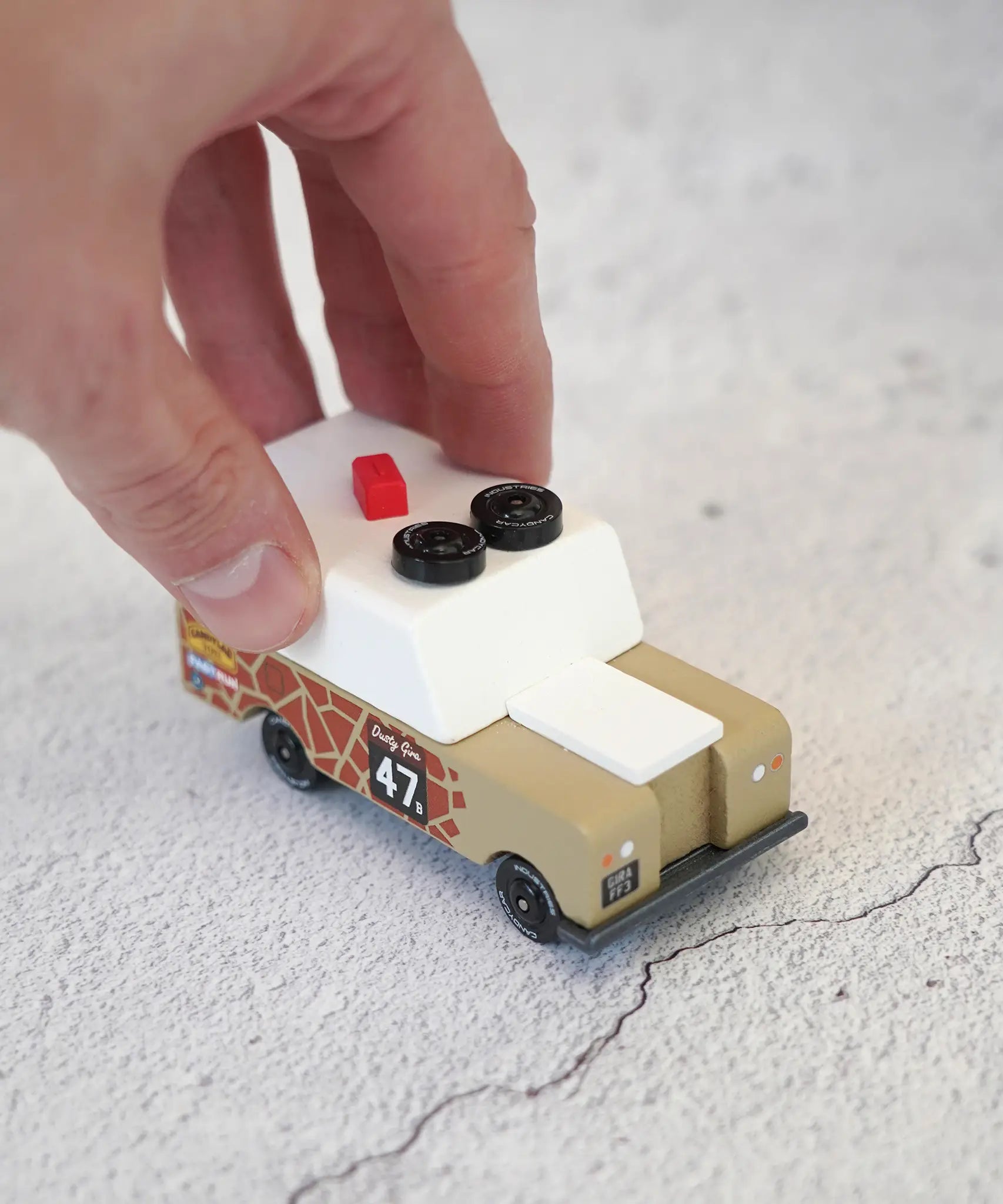 Adult hand pushing the Candylab wooden diecast safari Gira drifter adventure toy truck showing scale