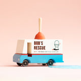 Candylab toy plumbing truck on a pink faded background next to a small blue puddle