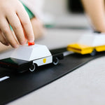 Close up of a childs hand pushing the candylab candycar police vehicle on a black rubber road