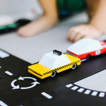 Close up of a child playing with the Candylab wooden taxi toy car on a black toy road set