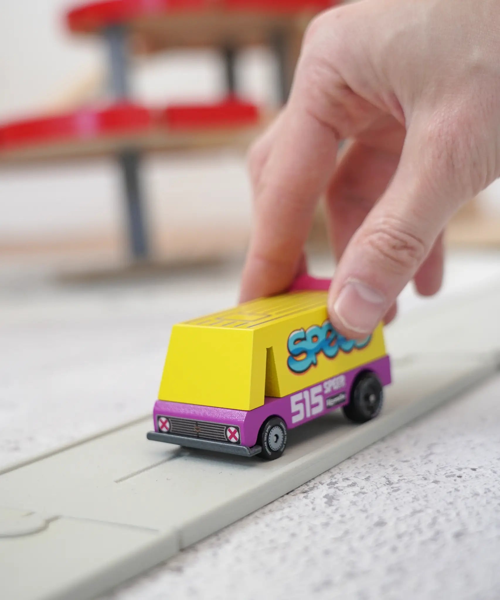 Adult hand holding a Candylab wooden diecast yellow speed vandal toy van showing scale