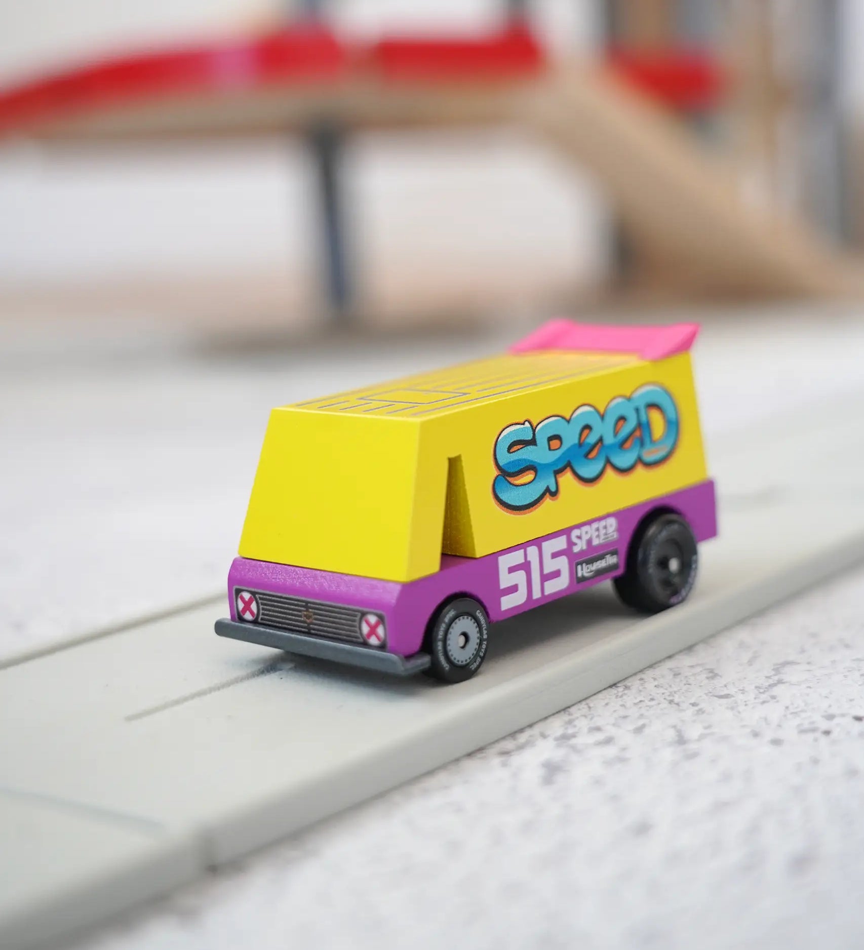 A Candylab wooden diecast yellow speed vandal toy van with a pink spoiler and decals on a playroad