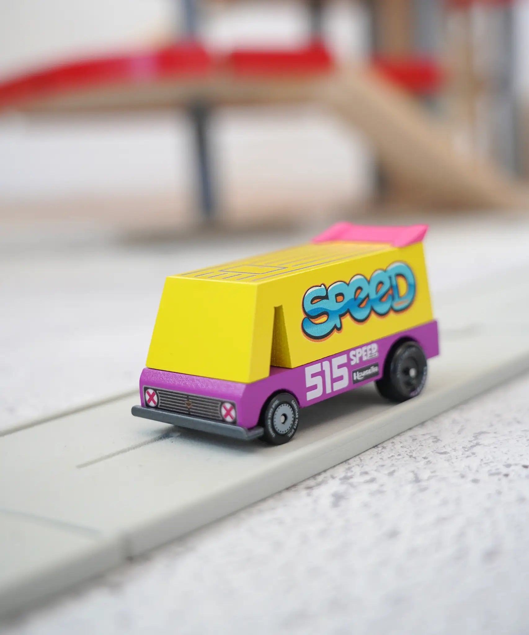 A Candylab wooden diecast yellow speed vandal toy van with a pink spoiler and decals on a playroad