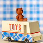 CandyLab cream and blue CandyVan with a brown teddy bear on the roof with Toys text logo in red on the side - on a table with a blue check blanket in the background.