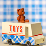 CandyLab cream and blue CandyVan with a brown teddy bear on the roof with Toys text logo in red on the side - on a table with a blue check blanket in the background.