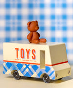 CandyLab cream and blue CandyVan with a brown teddy bear on the roof with Toys text logo in red on the side - on a table with a blue check blanket in the background.
